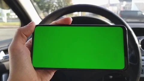 The driver holds a smartphone with a green screen horizontally behind the wheel Stock Footage 294098933