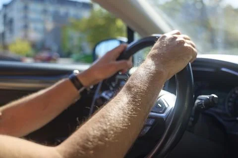 Driver holds steering wheel with both hands inside car on sunny city street Stock Photos
