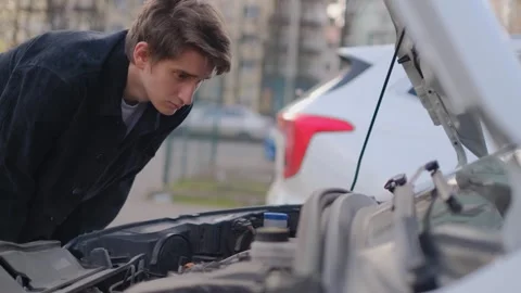 A driver looks under the hood of a broken car trying to figure out what's wrong Stock Footage 304007065
