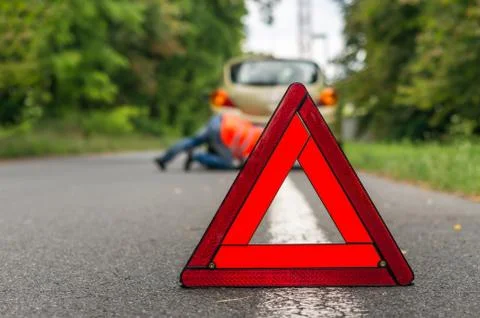 Driver lying under the broken car and traffic warning triangle Foto stock