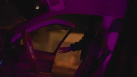 Driver in neonlit vehicle checks mirror, Urban night scene with driver adjusting Stock Footage 329452938