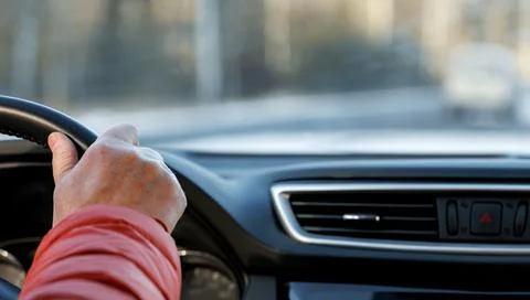 A driver in an orange jacket on the steering wheel inside the car. Foto stock