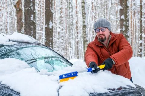 Driver preparing car for trip, man cleaning snow from hood with brush in wi.. Stock-Fotos