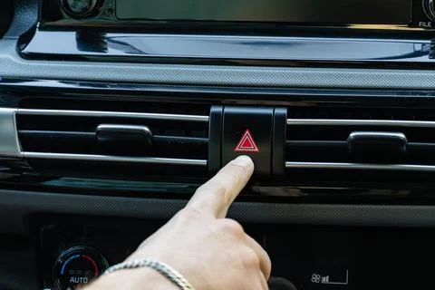 Driver pressing hazard warning lights button on car dashboard Stock Photos