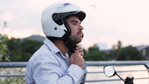 The driver pulls on his helmet while balanced on the stationary moped. Stock Footage 312800648