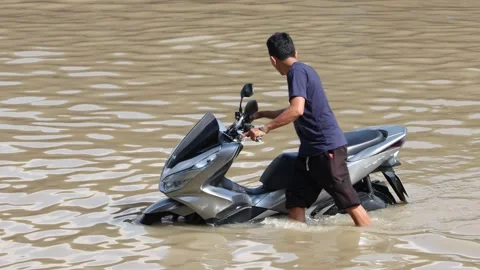 Driver pushes motorcycle through flooded street Stock Footage 345057630