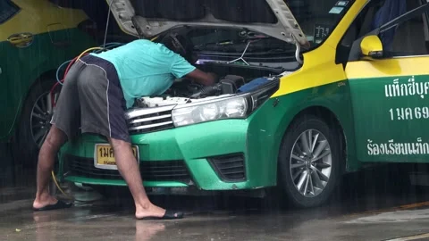 Driver repairs taxi engine in rainy weather at city taxi station Stock Footage 310559477