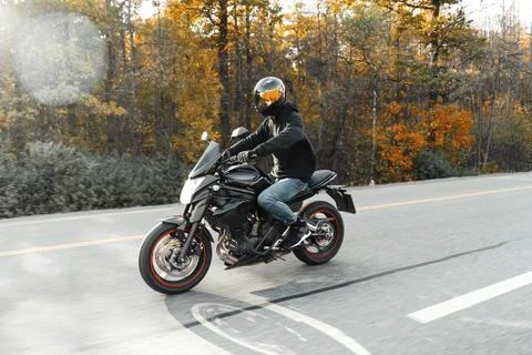 Driver riding motorcycle on empty road in beautiful autumn forest. Stock-Fotos