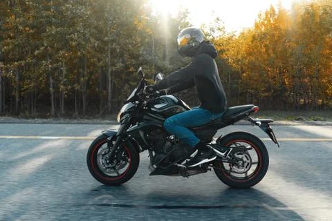 Driver riding motorcycle on empty road in beautiful autumn forest. Stock Photos