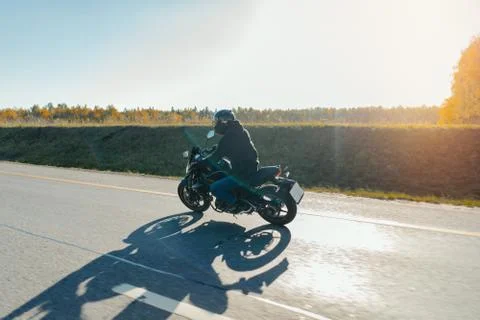 Driver riding motorcycle on empty road in beautiful autumn forest. Foto stock