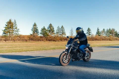 Driver riding motorcycle on empty road in beautiful autumn forest. Stock Photos