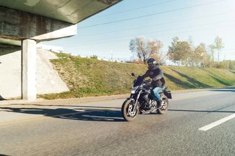Driver riding motorcycle on empty road out of the city at beautiful autumn time. Stock Photos