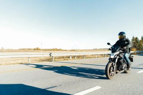 Driver riding motorcycle on empty road out of the city at beautiful autumn time. Stock Photos