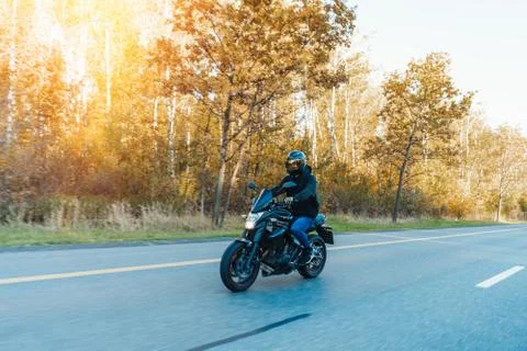 Driver riding motorcycle on empty road in beautiful autumn forest. Stock Photos