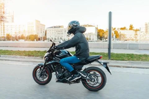 Driver riding motorcycle on empty road in beautiful autumn city. Stock Photos