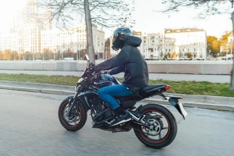 Driver riding motorcycle on empty road in beautiful autumn city. Stock Photos