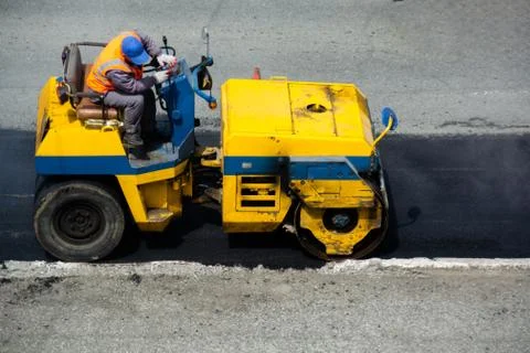 Driver of road roller leveling new layer of asphalt. Not large machine in yel Foto stock