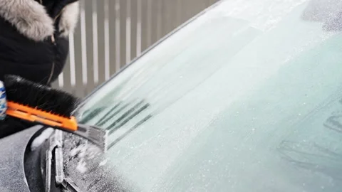 Driver scrapes thick ice off a car windshield with an orange ice scraper brush Stock-Footage 328133051