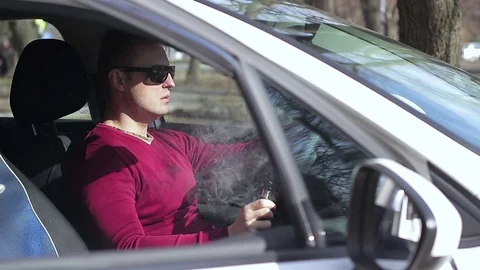 The driver smokes an electronic cigarette in the car and looks at the came Stock Footage 73989083