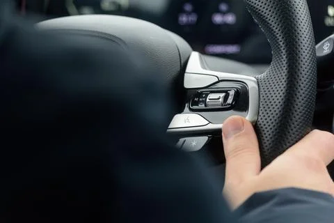 Driver thumb adjusts steering wheel media controls to keep eyes on road and Stock Photos