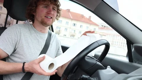 Driver urgently searches for a restroom while holding toilet paper in his car Stock Footage 343720461