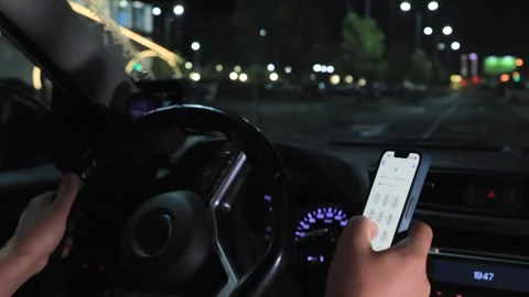 Driver using smartphone while driving car at night in city street traffic Stock Footage 316808089