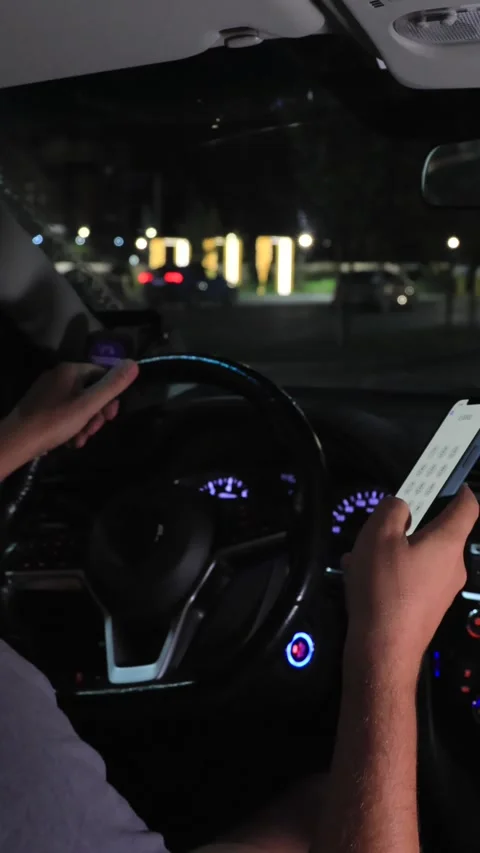 Driver using smartphone while driving car at night in city street traffic Stockbeeldmateriaal 316808139
