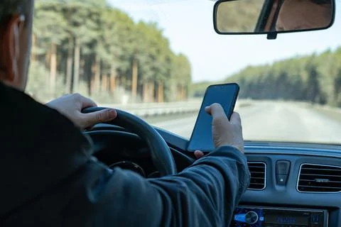 A Driver Using a Smartphone While Navigating a Scenic Road Surrounded by Tree Stock Photos