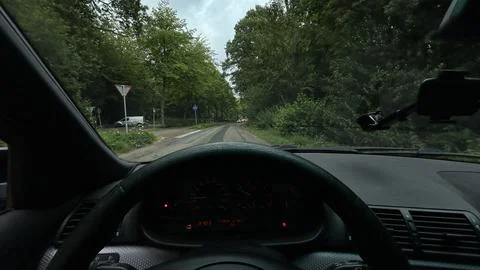 Driver view of narrow tree-lined road from car cockpit under overcast sky Stock Photos