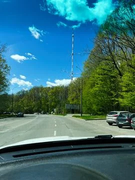 Driver view of a suburban road lined with spring forest and a tall radio to.. Stock Photos