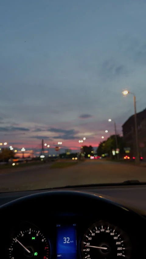 Driver view through windshield on city street at dusk with glowing streetlights Stock Footage 345124311