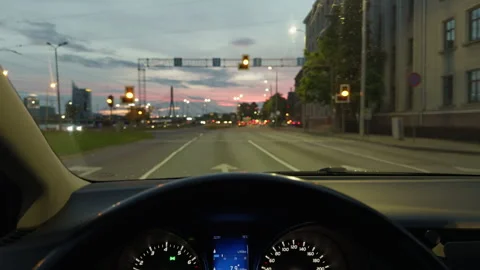 Driver viewpoint inside moving car on city street at dusk with glowing dashboard Stock Footage 344990896