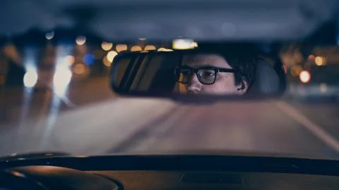Driver's face is reflected in a rear view mirror, night shot Foto stock