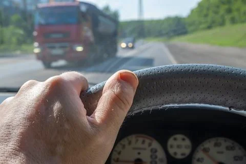 Driver's hand on the steering wheel of a car and a passing truck Stock Photos