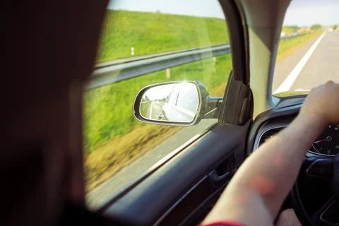 Driver's hand on steering wheel inside a car, view of side mirror reflecting Foto stock