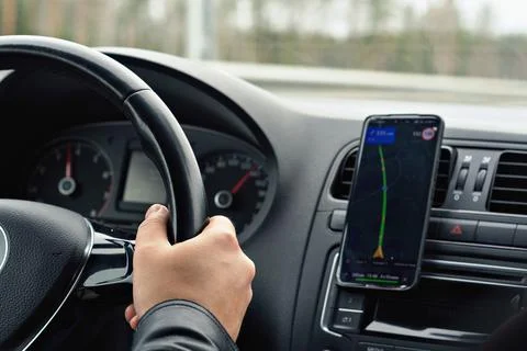 Driver's hand on steering wheel with navigation app on smartphone, illustrati Stock Photos