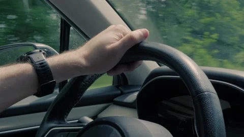 A driver's hand wearing a black watch holds the steering wheel of a moving .. Video stock 341324062