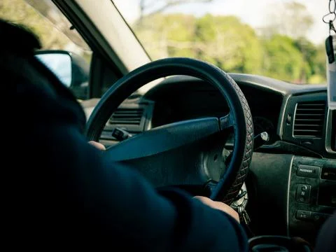 Driver's hands on a black steering wheel inside a car Stock Photos