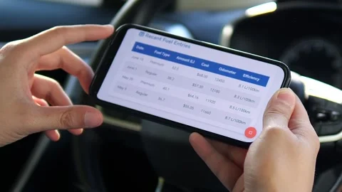 A drivers hands hold a phone displaying a fuel cost tracking application Stock Footage 315672023