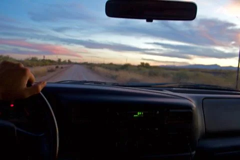Drivers point of view of a drive on a dirt road after sunset, one hand on the Stock Photos