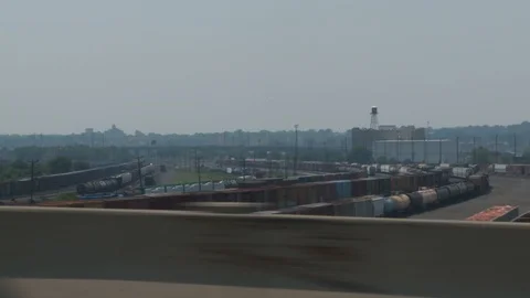 Driving along highway with freight train station and buildings in distance, day. 스톡 동영상 107990432
