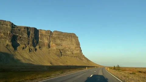 Driving along Iceland Ring Road beneath towering basalt cliffs in golden Stock Footage 345969043