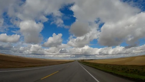 Driving along a rural old paved road through flat ranch land under a blue sky Stock Footage 295369339