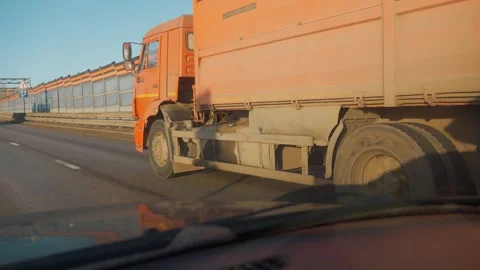 Driving alongside a large orange dump truck on a highway 库存影片 334758616