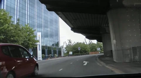 Driving beneath flyover in shadow of carriageway past glass fronted offices Stock Footage 12180652
