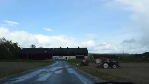 Driving on bumpy country lane past acre with tractors on rainy sppring day Video stock 166170255