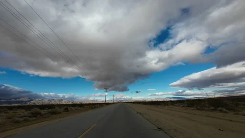 Driving down an empty Mojave Desert road on an overcast day with utility Stock Footage 167929076