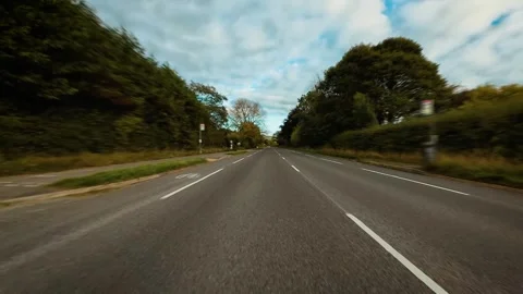 Driving on empty countryside road surrounded by green trees under cloudy sky POV Stock Footage 335816926