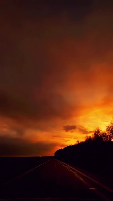 Driving on Empty Road at Dramatic Sunset with Fiery Sky and Dark Silhouettes Vídeo Stock 331993004