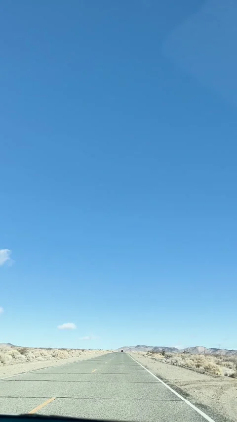 Driving an empty road stretched through a desert landscape during a sunny day Stock Footage 286729143